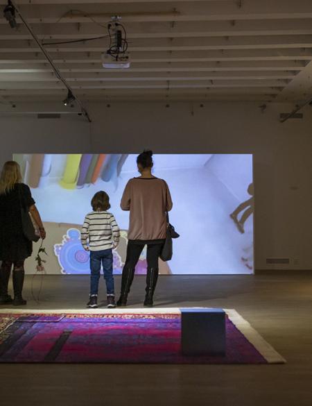 zdjęcie ukazuje ludzi w salach galerii oglądających film wideo na dużym ekranie